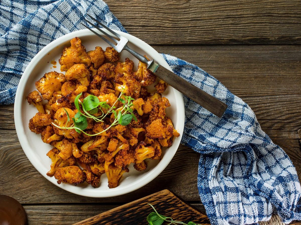 Ein knuspriges veganes Blumenkohl-Gyros aus dem Ofen auf einem großen weißen Teller mit Kräutern garniert