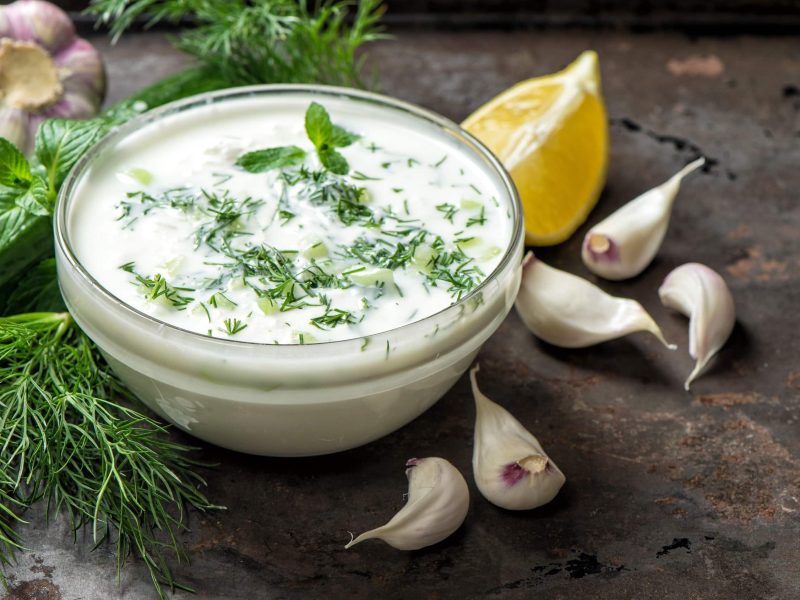 Eine große Schale mit veganem Tzaziki mit Zitrone, Kräutern, frischem Knoblauch und saftiger Gurke auf einem steinernen Tisch