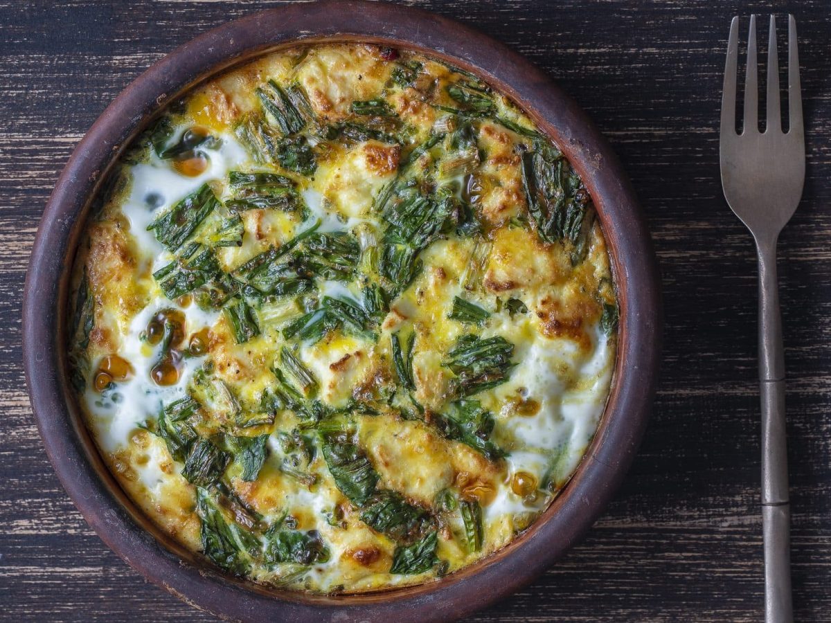 Aus der Vogelperspektive: Auf einer dunklen Holzplatte steht eine Keramkschüssel, in der eine Vegetarische Bärlauch-Frittata ist.