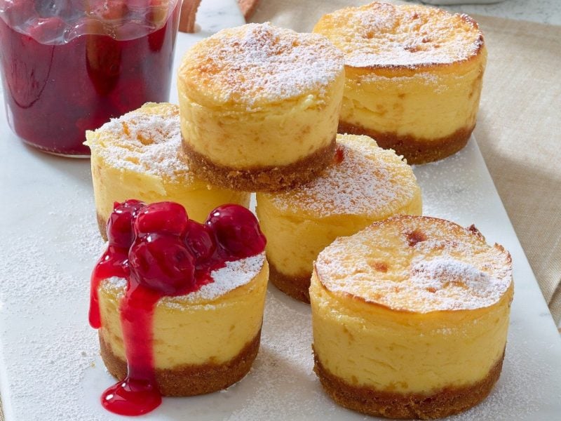 Unsere Cheesecake-Törtchen mit Kirch-Mousse stehen in Reih und Glied auf einer weißen Platte auf dem Tisch.