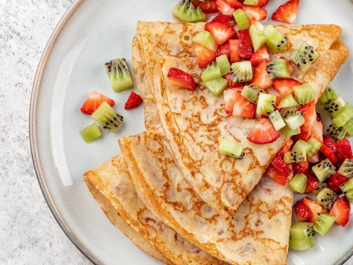 Unsere Crêpes mit Erdbeer-Kiwi-Salat liegen fein angerichtet auf einem Teller.