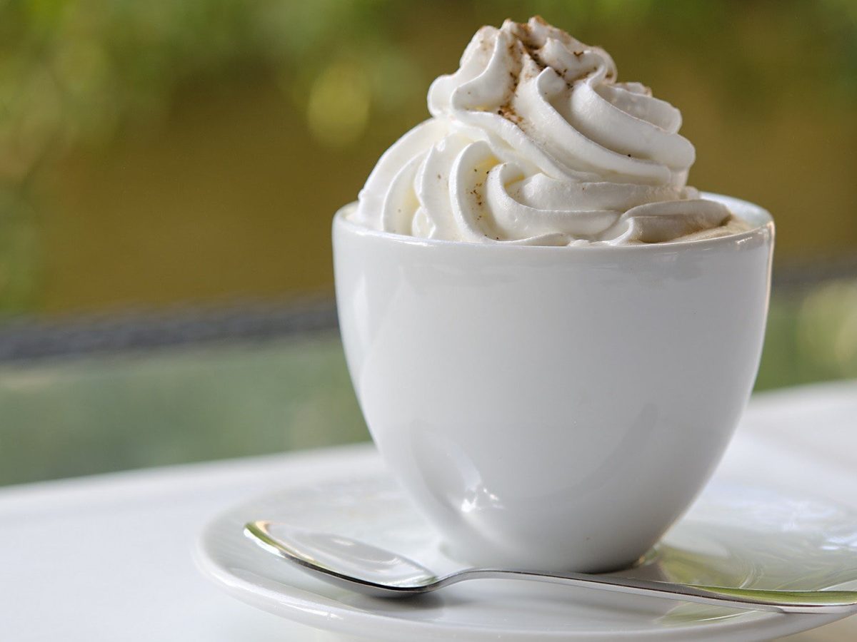 Auf einem Unterteller steht eine Tasse High-Tea wie im Londoner des 19. Jahrhunderts. Genieße diesen Earl Grey mit whipped Cream und träume von deinem Leben am englischen Königshof. Auf der Creme oben drauf ist etwas Kakaopulver.