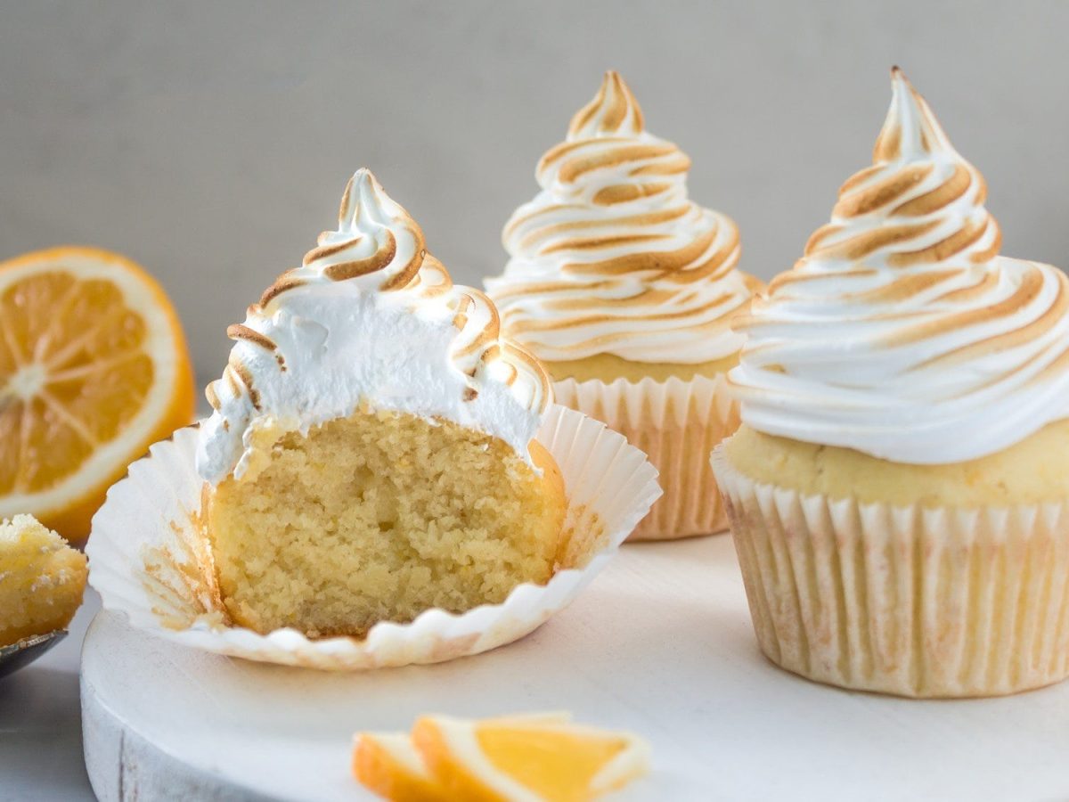 Auf einem Holzteller stehen drei Meringue Cupcakes. Sie sind mit Meringue Creme dekoriert. Die Creme ist karamellisiert.