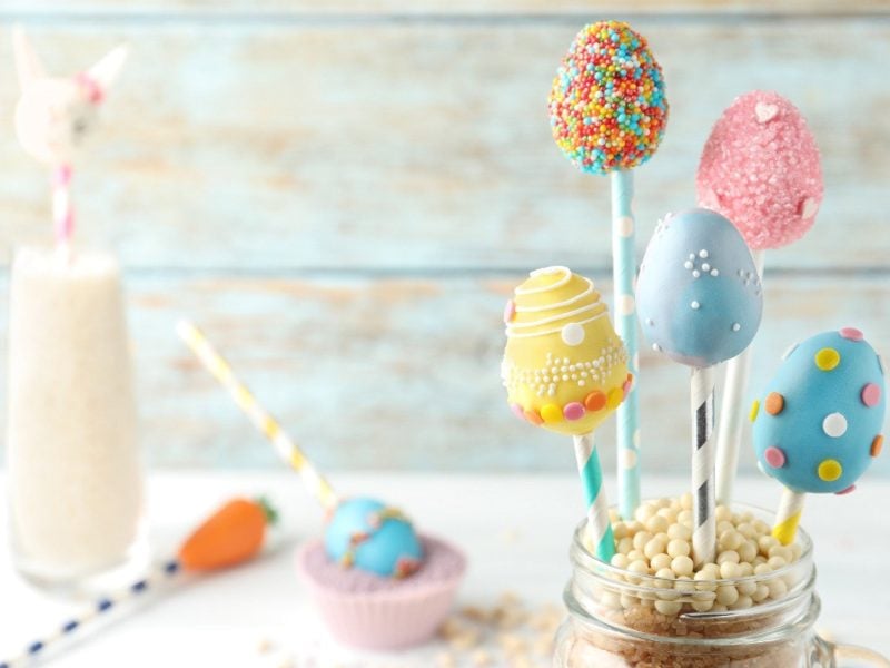 In einem Einmachglas stehen fünf Oster-Cakepops am Stiel. Sie sind in unterschiedlichen Farben dekoriert und mit Streuseln bestreut.