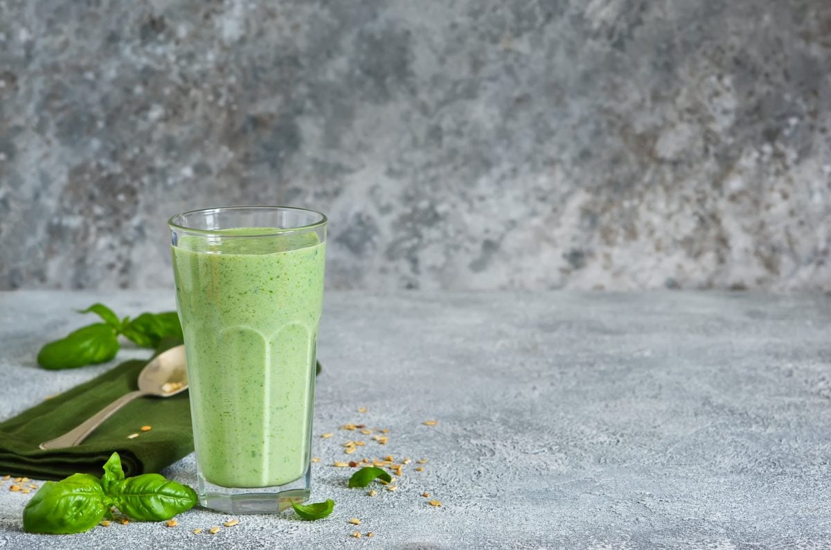 Ein volles Glas von unserem Smoothie mit Basilikum und Chiasamen steht auf grauem Steinboden.