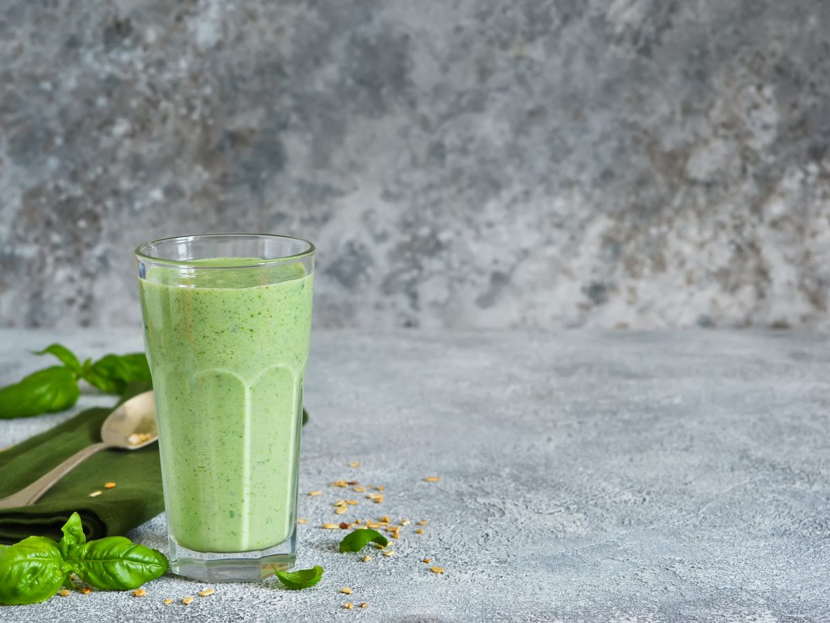 Ein volles Glas von unserem Smoothie mit Basilikum und Chiasamen steht auf grauem Steinboden.