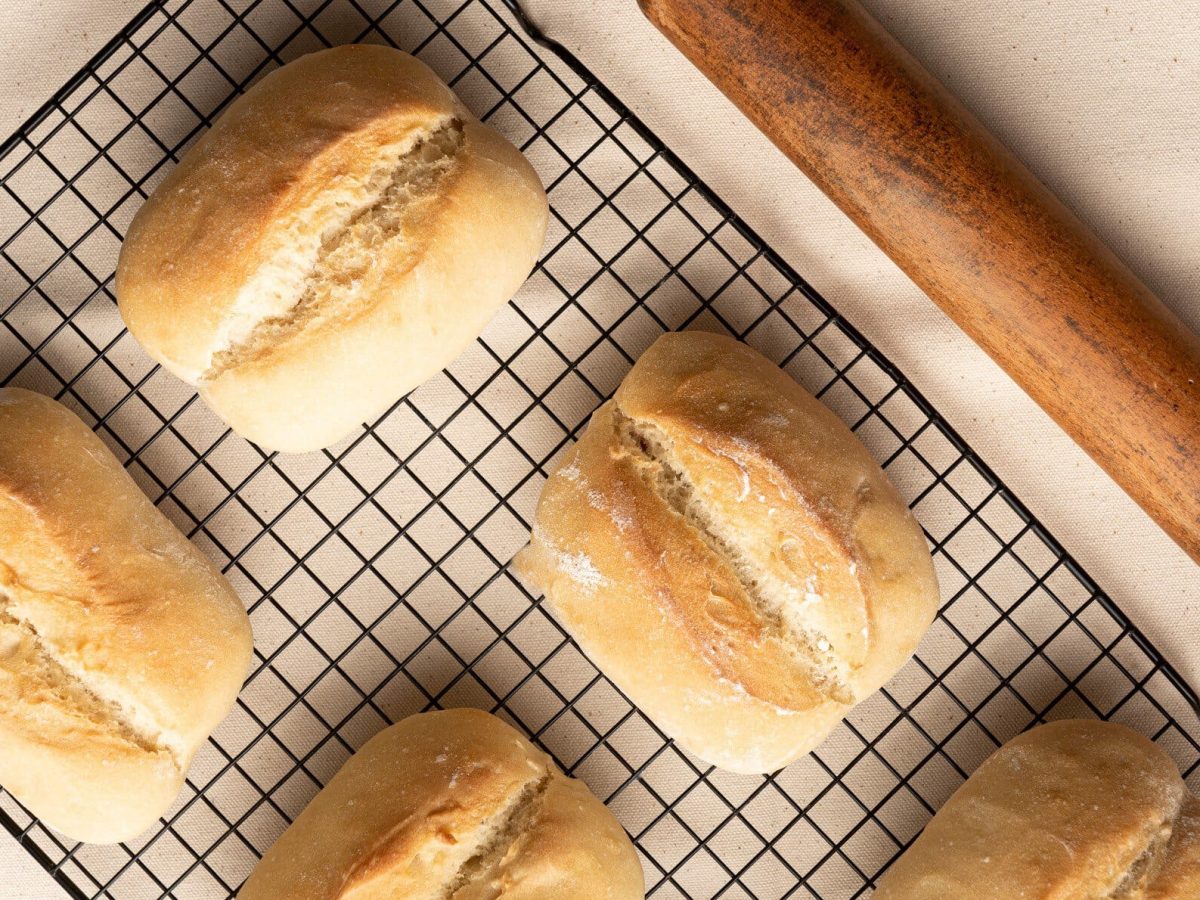 Auf einem Ofengitter liegen mehrere selbstgemachte Brötchen ohne Gluten. Sie sind goldbraun gebacken.