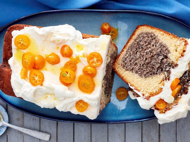 Unser Mohn-Joghurt-Kuchen liegt angeschnitten auf einer Kuchenplatte. Zwei Stücke sind abgeschnittenn.