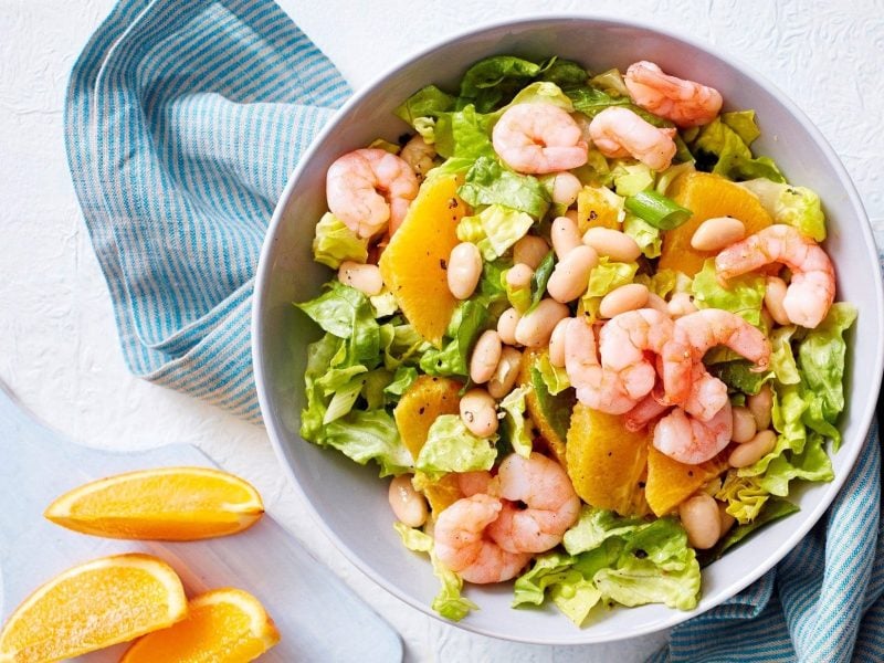 Eine Schüssel mit unserem Orangensalat mit Garnelen steht auf einem Serviertuch auf dem Tisch.