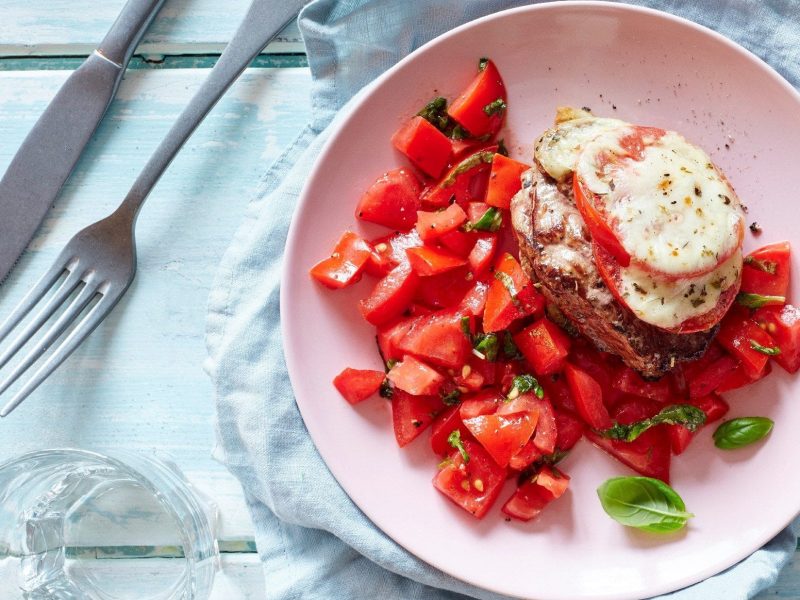 Unser Pizzaiola-Steak liegt fein angerichtet mit Tomatensalat auf einem rosa Teller zum Verzehr bereit.