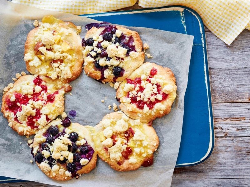 Unsere Streuseltaler-Tarte liegt angerichtet auf Butterbrotpapier auf einem blauen Holzbrett.