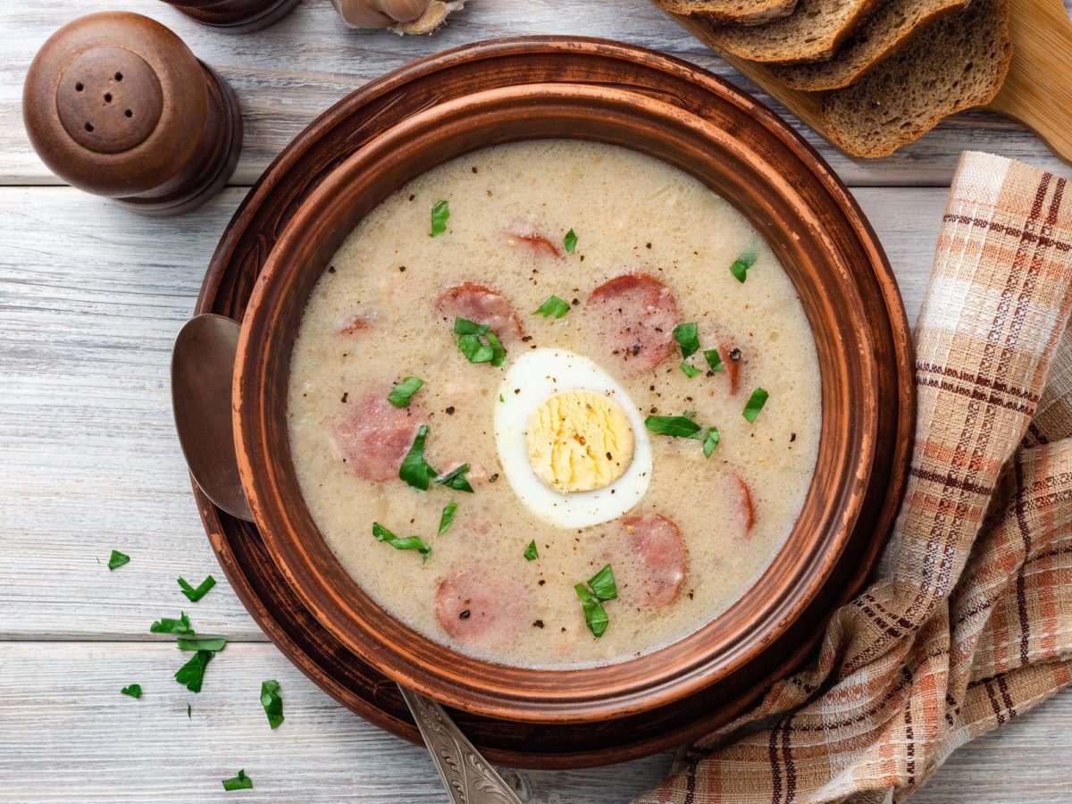 Polnische Ostersuppe Zurek in Tonschüssel auf hellem, hölzernen Untergrund.