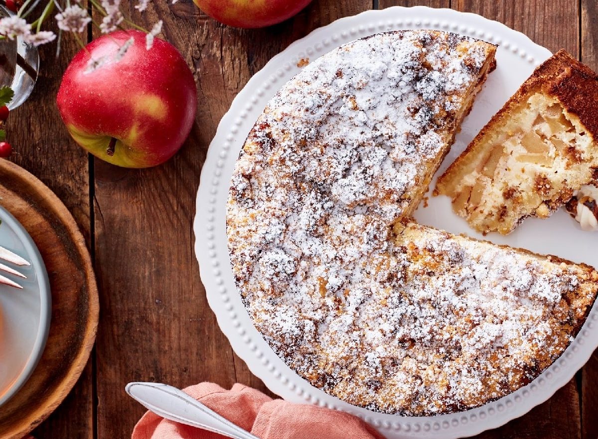 Apfel-Müslikuchen mit Puderzucker bestäubt auf einer Kuchenplatte auf einem dekorierten Holztisch