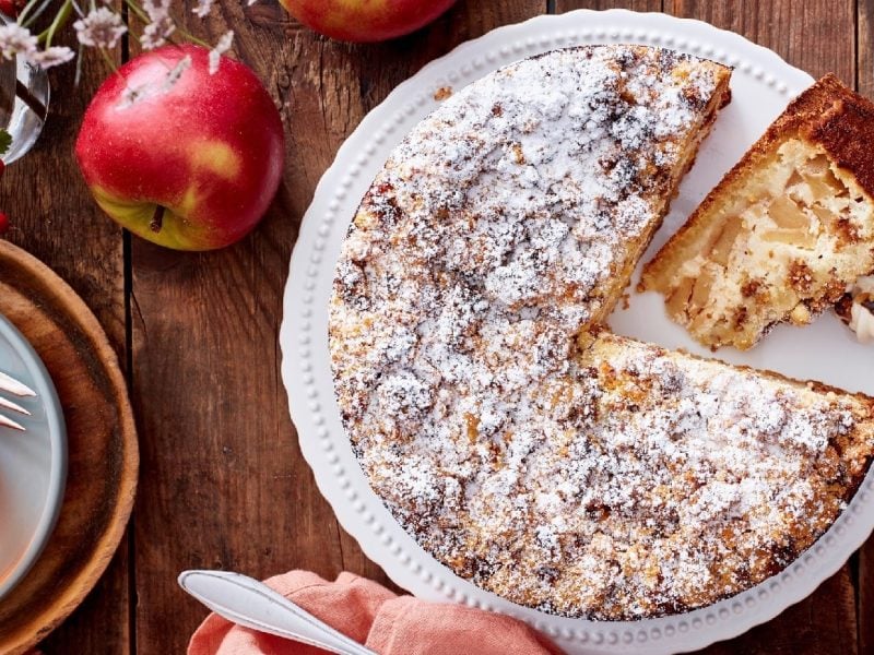 Apfel-Müslikuchen mit Puderzucker bestäubt auf einer Kuchenplatte auf einem dekorierten Holztisch