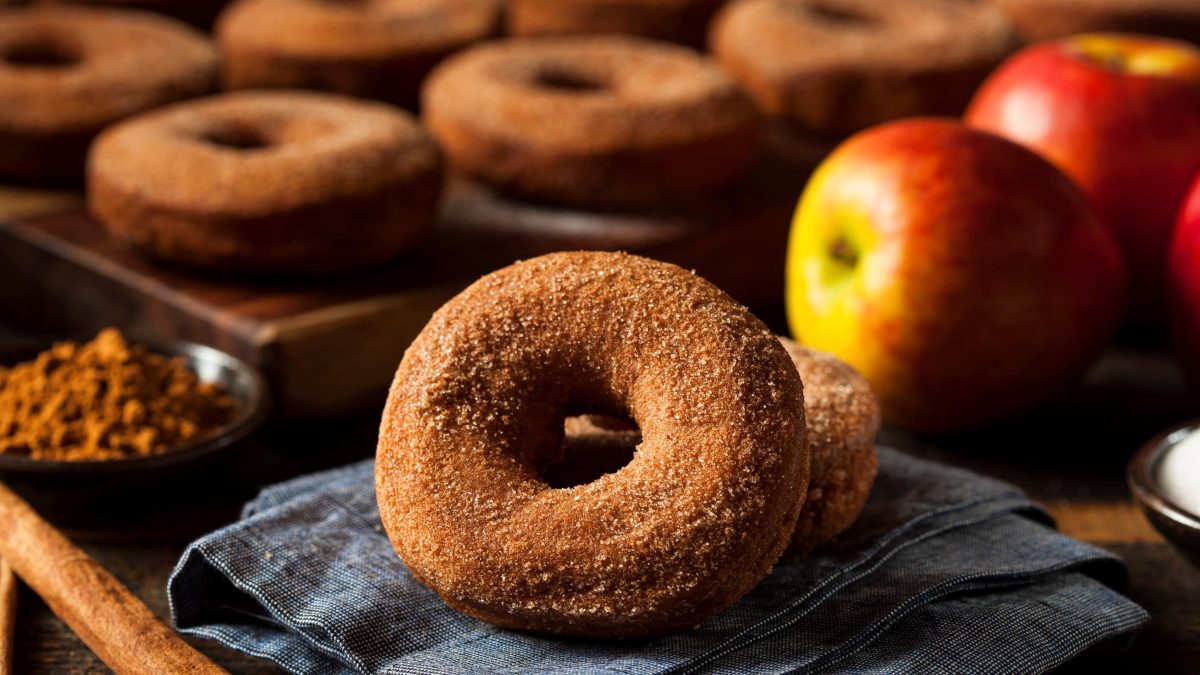 Mehrere braun bestäubte Donutzs auf einem Gitterblech mit einem frischen Apfel.