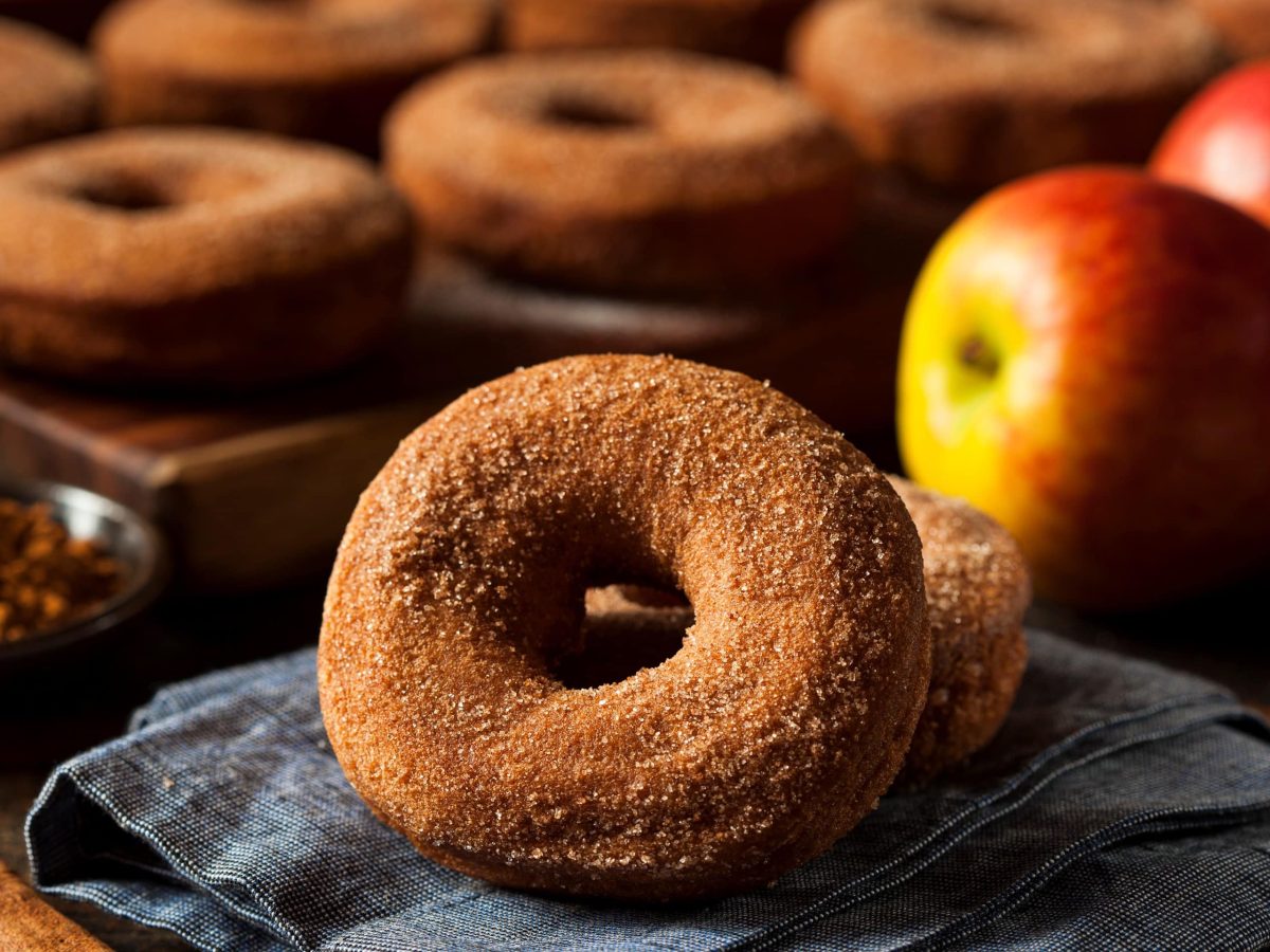 Mehrere braun bestäubte Donutzs auf einem Gitterblech mit einem frischen Apfel.