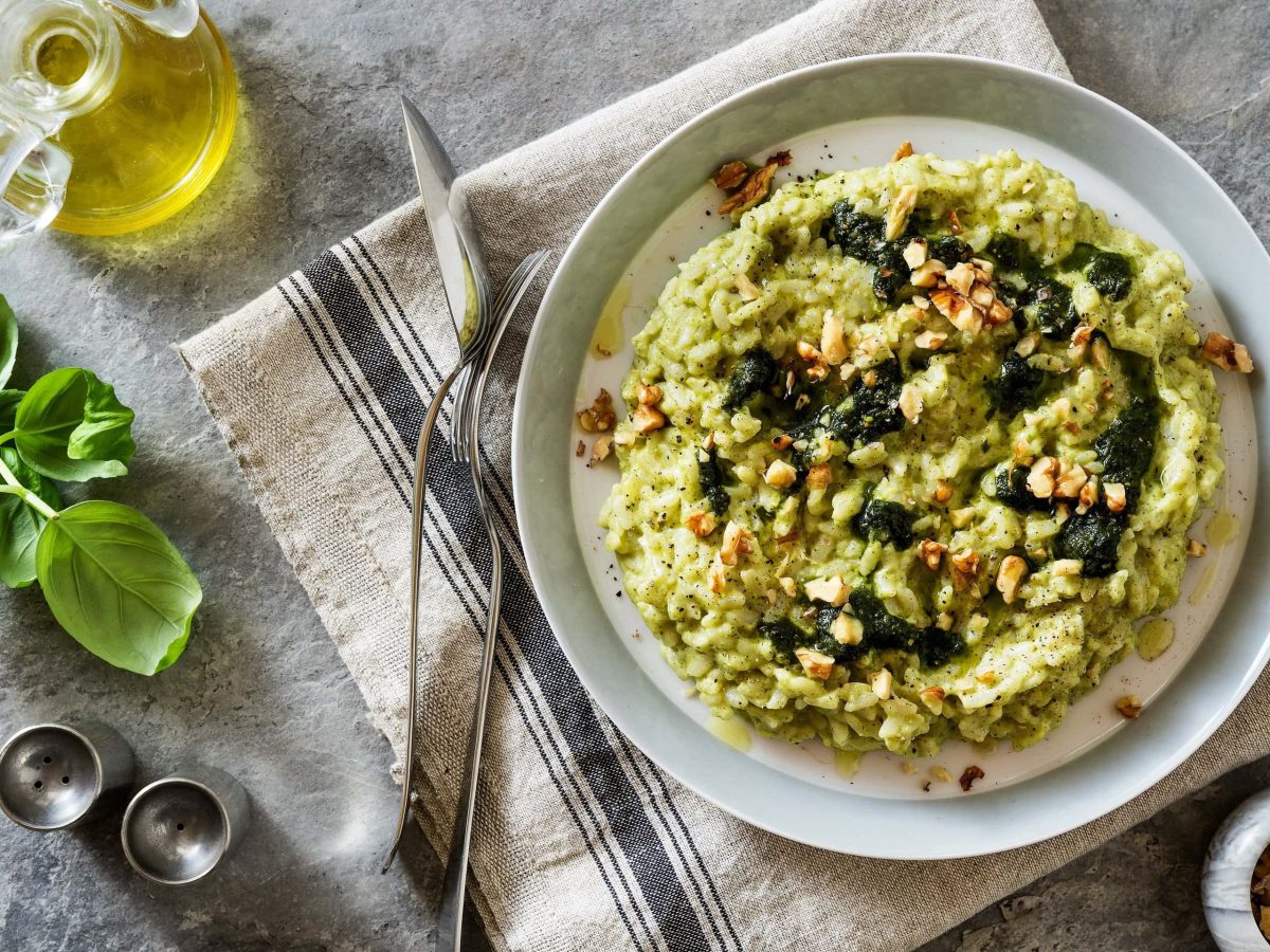 Ein Teller Bärlauch-Risotto mit Walnüssen in der Draufsicht, daneben Zutaten wie Weißwein und Nüsse.