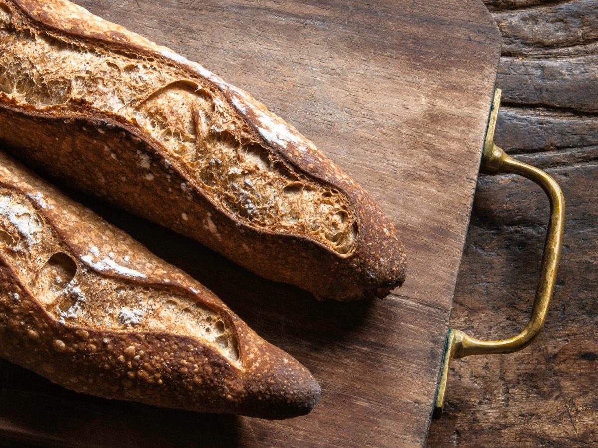 Zwei original Französische Baguettes auf Holzbrett und Holztisch. Aufnahme aus der Vogelperspektive.