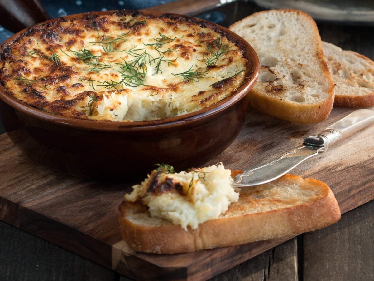 Auflaufform mit Brandade auf Holzbrett und Weißbrot mit dem Fischpüree.