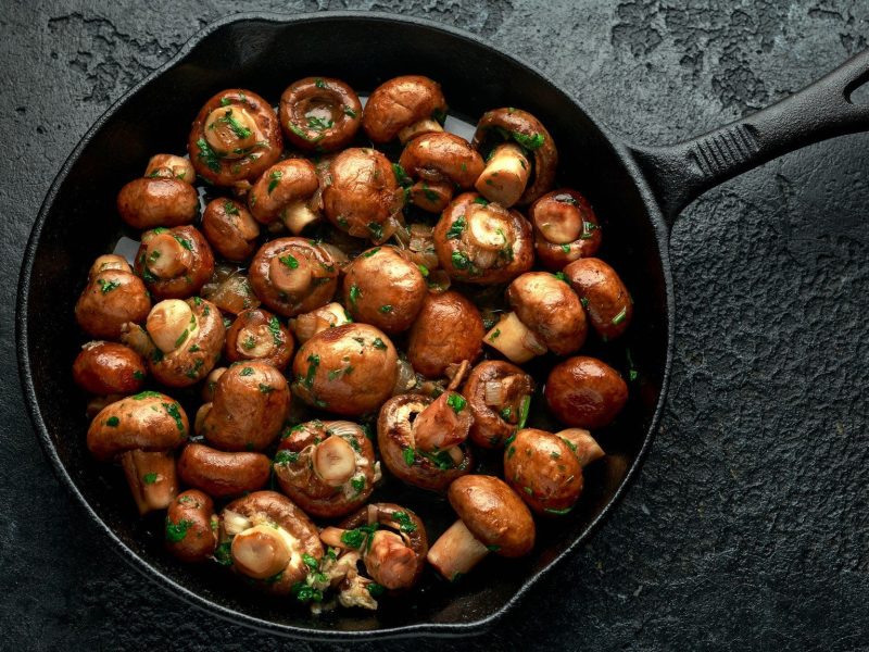 Eine Pfanne Champignons mit Sherrysauce auf dunklem Untergrund in der Draufsicht.