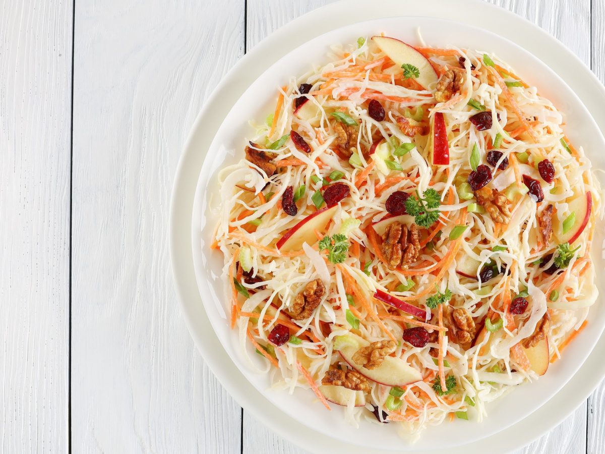 Ein Teller Coleslaw mit Äpfeln und Walnüssen auf hellem Holz in der Draufsicht.