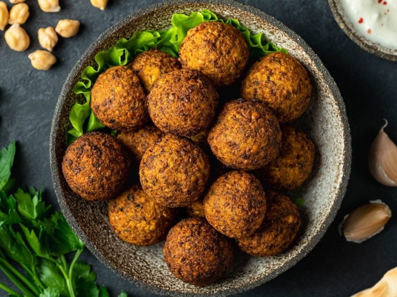 Eine Schale Falafel mit Erdnüssen in der Draufsicht, daneben eine Schüssel Joghurt, Kräuter und Kichererbsen.