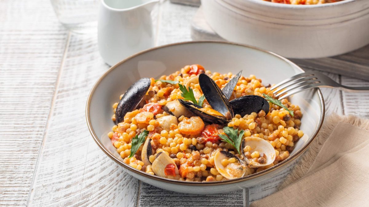 Schale Fregola mit Meeresfrüchten auf weißem Tisch