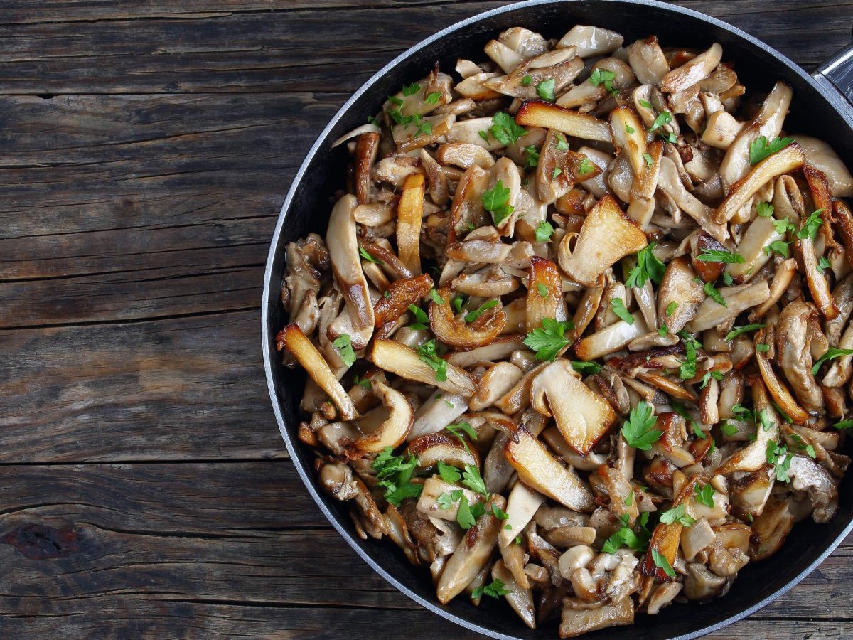 Eine Pfanne mit italienischer Antipasti: Funghi Trifolati mit Petersilie und Knoblauch in einer großen Pfanne auf hölzernem Untergrund, von oben fotografiert.