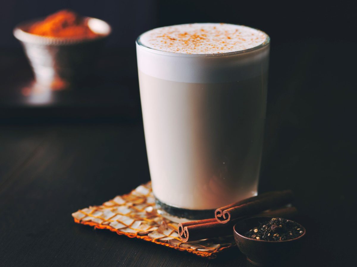 Ein Glas Goguma Latte mit Milchschaum und Zimt bestreut auf dunklem Untergrund.