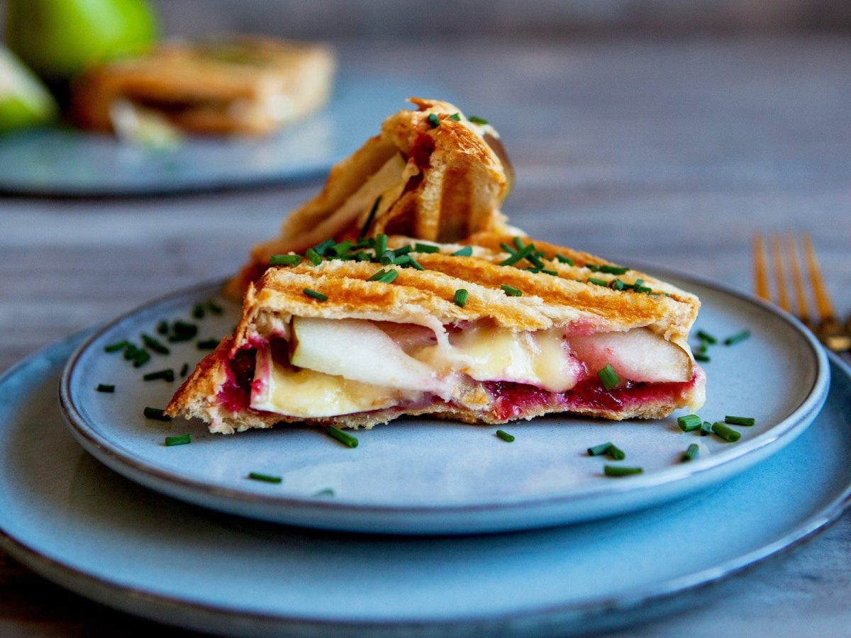 Grilled Cheese Sandwich mit Birne auf einem blauen Teller. Im Hintergrund verschiedene Zutaten.