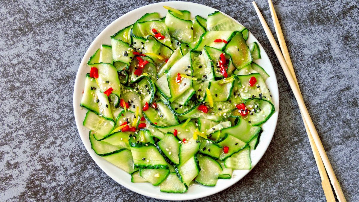 Ein Teller Gurkensalat mit Orangendressing und Chili und Sesam, daneben liegen Essstäbchen.