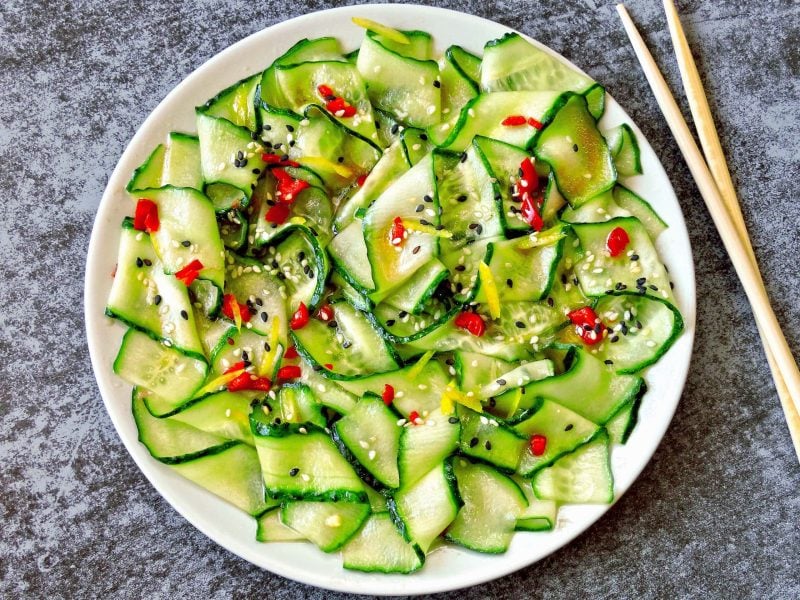 Ein Teller Gurkensalat mit Orangendressing und Chili und Sesam, daneben liegen Essstäbchen.