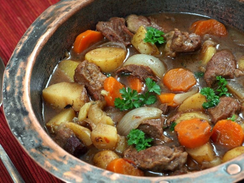 St. Patrick's Day Irish Stew in traditionellem Teller aus Steingut auf Holztisch. Daneben antiker Silberlöffel. Draufsicht.