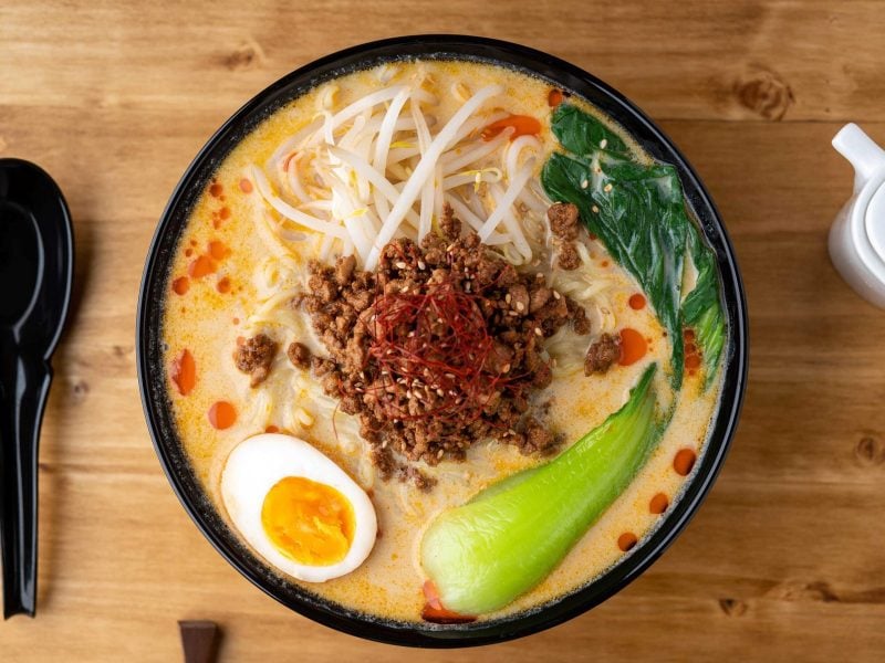 Japanische Nudelsuppe mit Ei, Hackfleisch, Nudeln, Pak Choi und Sojasprossen in einer Schüssel mit Löffel.