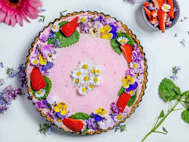 Aus der Vogelperspektiv: Auf einem hellblauen Untergrund steht Kuchen mit Erdbeeren und ganz vielen kandierten Blüten.