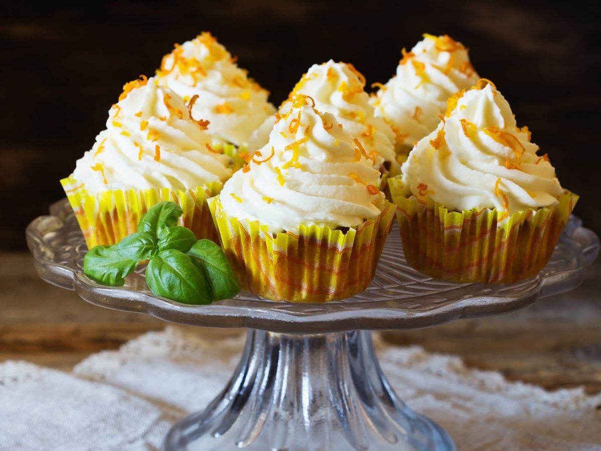 Ein Tortenständer, auf dem sechs Möhren-Cupcakes mit Orange stehen.