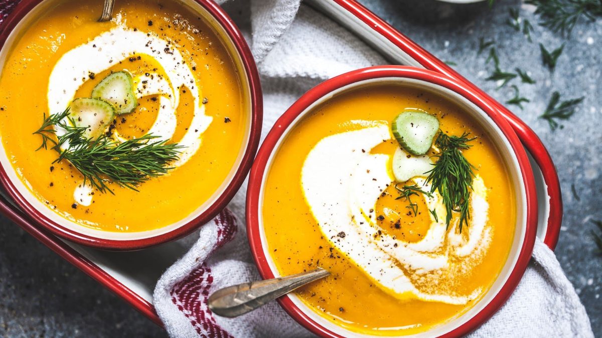 Zwei Schüsseln Möhren-Fenchel-Suppe mit Fenchelgrün, Crème fraîche und Fenchelstängeln in der Draufsicht.