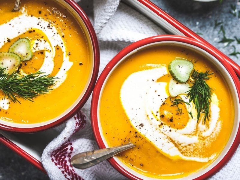 Zwei Schüsseln Möhren-Fenchel-Suppe mit Fenchelgrün, Crème fraîche und Fenchelstängeln in der Draufsicht.