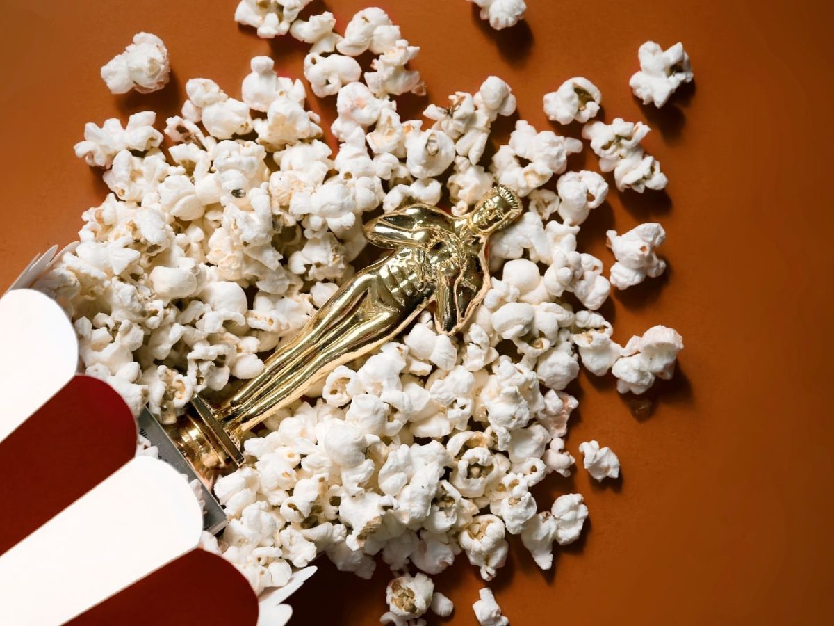 Ein eumgefallene Tüte Popcorn mit der liegenden Oscar Statue auf einem orange-braunem Untergrund.