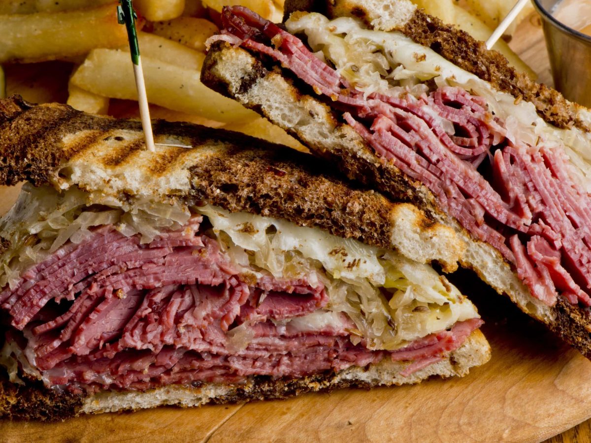 Angeschnittenes Reuben Sandwich von der Seite mit Pommes im Hintergrund auf Holztisch