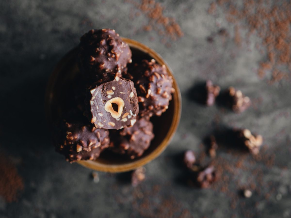 Selbstgemachte Rocher in einer Holzschale auf dunklem Untergrund mit Kakaopulver.