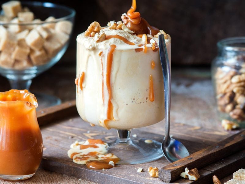 Salted Caramel Milkshake auf einem Holzbrett. Daneben verschiedene Zutaten.