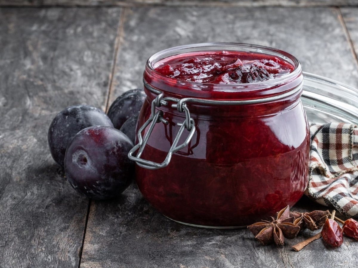 Selbst gemachtes Pflaumen-Chutney mit Nelken und Sternanis, in einem Marmeladenglas, serviert auf einem hölzernen, grauen Tisch.