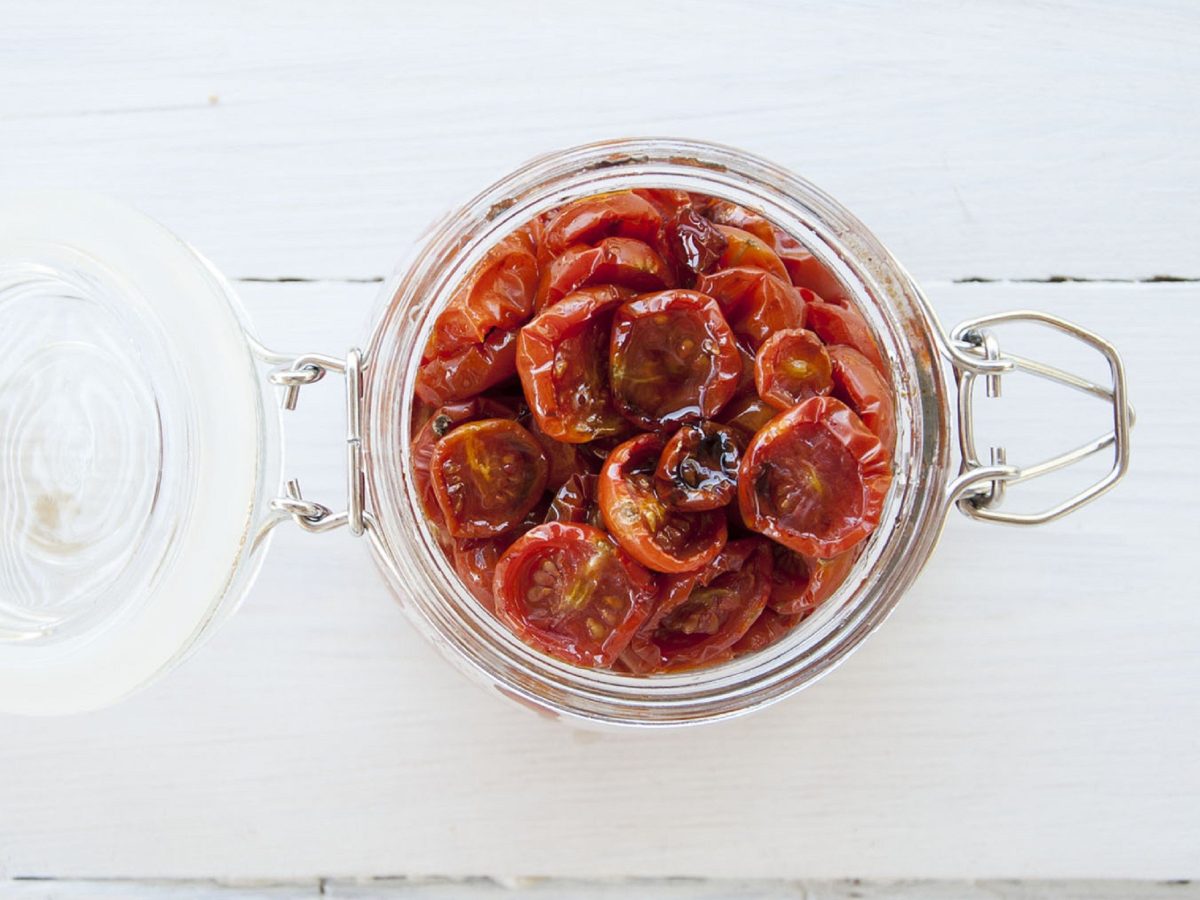 Selbst getrocknete Tomaten in einem offenen Glas aus der Vogelperspektive aufgenommen, auf einem hellen Holztisch.