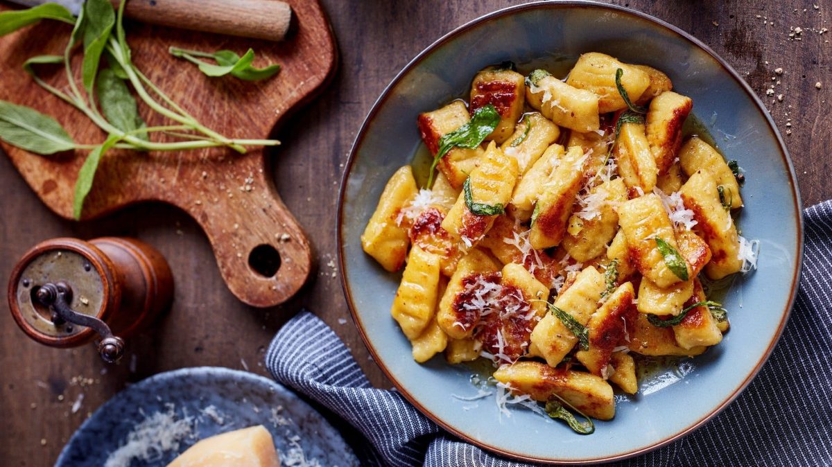 Ein Teller von unseren selbst gemachten Gnocchi mit Salbeibutter steht auf einem braunen Holztisch.