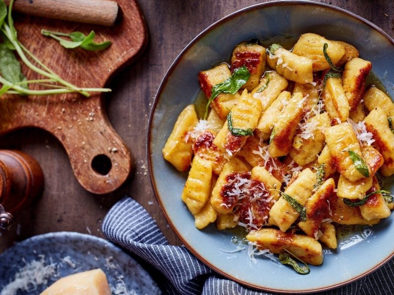 Ein Teller von unseren selbst gemachten Gnocchi mit Salbeibutter steht auf einem braunen Holztisch.