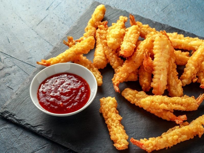 Shrimp Tempura auf einer Schiefernplatte. Daneben eine schale mit süß-saurer Sauce.