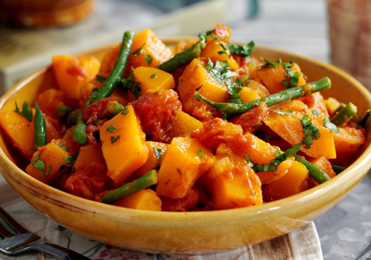 Eine Schüssel Süßkartoffelcurry mit grünen Bohnen und frischen Kräutern.