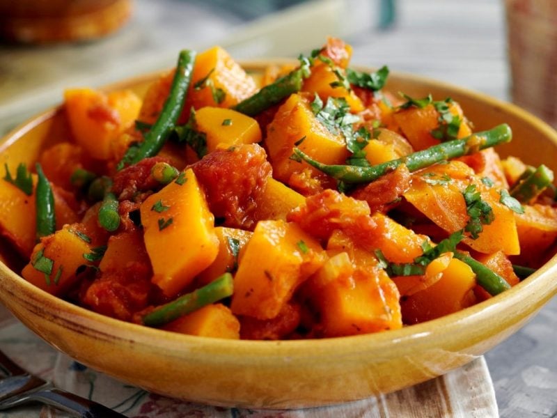 Eine Schüssel Süßkartoffelcurry mit grünen Bohnen und frischen Kräutern.