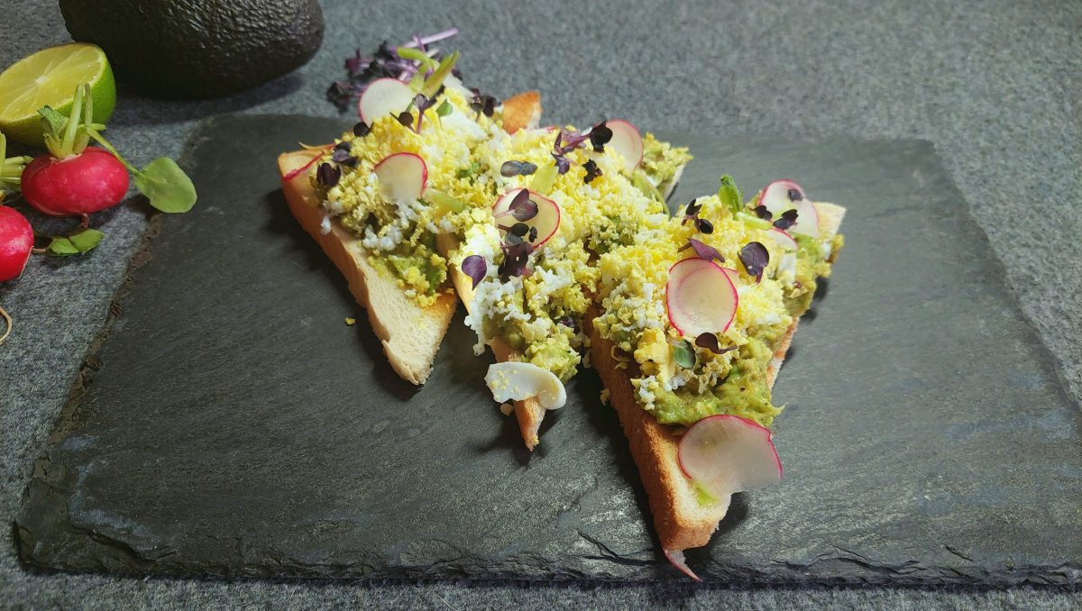 Avocado-Toast von oben mit geriebenem Ei auf schwarzer Schieferplatte